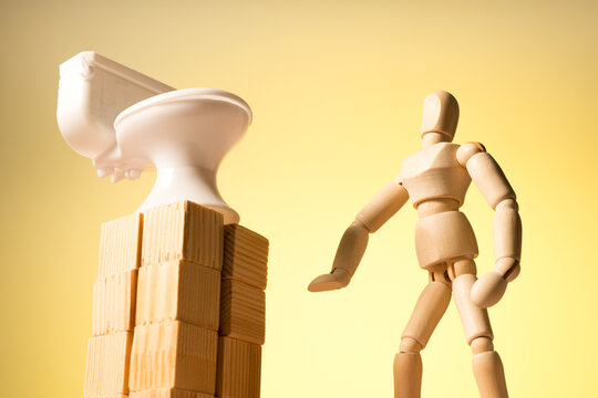 The toilet is on a pedestal and a wooden man is looking up at it