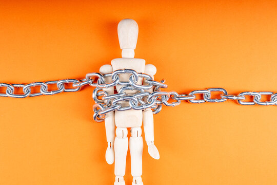 A wooden doll on an orange background is fixed with a chain