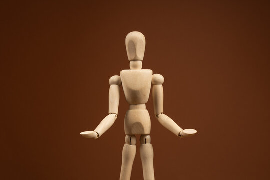 A wooden mannequin on a dark beige background stands with its arms spread out in different directions