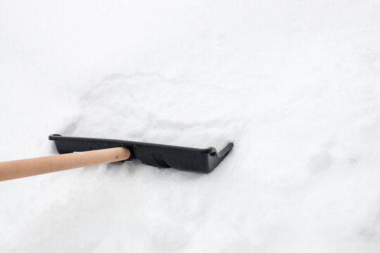 Snow shovel with wooden handle stuck in fresh snow after snowfall