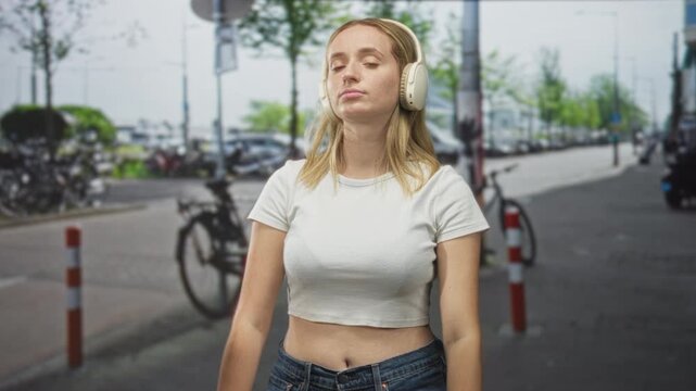 Woman wearing headphones makes timeout hand gesture and pursed lips on a city street with parked bicycles and bollards; annoyance reflection.