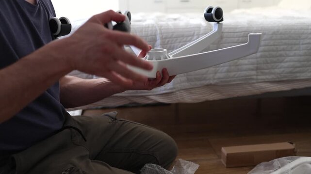 Adult male assembling office chair using hex key tool on wooden floor. Caucasian man hands screw chair lifting mechanism. Assembling office chair.