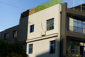 Obraz premium Architectural detail of a contemporary building's corner. The facade features a geometric play of light and shadow, off-white and grey walls, and striking blue window frames under a clear sky.