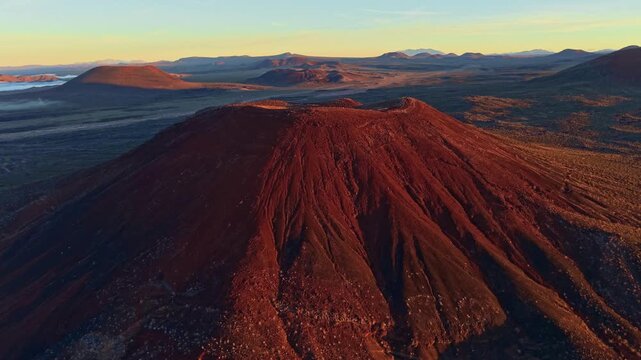 Scenic aerial perspective of volcanic cinder cones in Mojave Desert illuminated by golden sunrise light