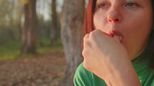Woman enjoys pastry. Female savoring pastry in forest scene. Woman relaxes outdoors with pastry under sunlit trees. Lady relishes her pastry during peaceful evening in sundappled forest setting