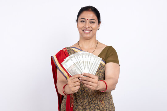 Indian happy rural village woman showing Indian 500 notes currency by looking at camera - concept of business profit, banking and agricultural sectors on white background