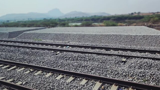 Angular, crushed stone ballast is stacked in rectangular blocks near rail tracks for construction or maintenance. These stockpiles allow for easy measurement, quality checks, & efficient distribution.