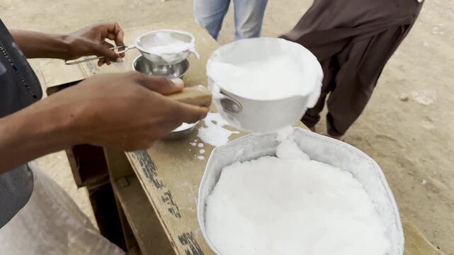 Close-up of fresh, frothy camel milk being strained into bowls for customers, followed by a wide shot of a traditional camel farm in a rugged desert landscape with majestic mountains in background.