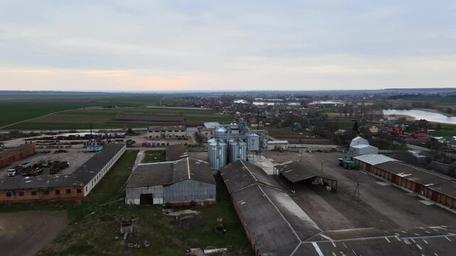 Aerial view of agricultural silos and grain elevators on a rural farm with barns and processing plant at sunset