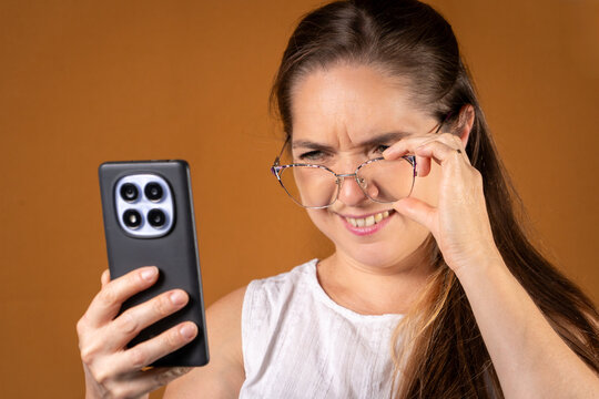 Mujer mirando su celular con dificultad, con una expresi&oacute;n de duda y problemas