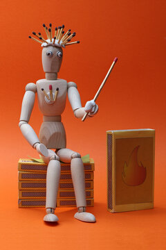 Still life with sitting wooden mannequin model, matchboxes and matches. Photo with maximum depth of field on orange background.