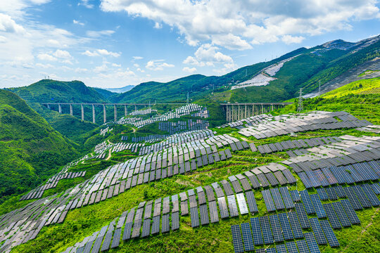 Large scale solar farm array integrated into mountain topography alongside a modern viaduct bridge.