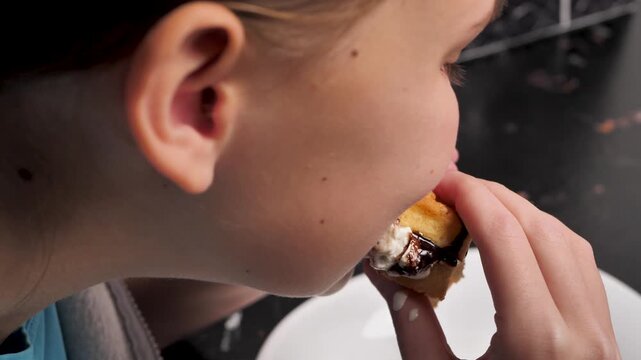 Young girl hungrily and greedily bites part of cake with cream and strawberry filling. Teenage girl eats waffle sandwich with cream, chocolate and berries filling. Sweet food with pastry and cream.