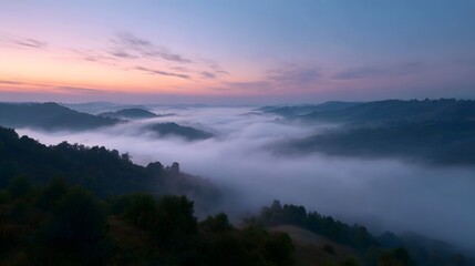 Obraz premium Rolling layered hills emerging from dense morning mist beneath a vibrant pastel dawn sky