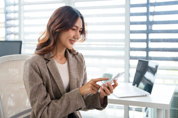 Fototapeta premium Happy busy young business woman using mobile phone, sitting at table in workplace, chatting , using app, enjoying online communication