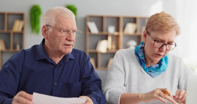 Senior couple budgeting retirement bills and taxes. They review paperwork, planning expenses at home to balance finances and savings. Concept is responsible household money management.