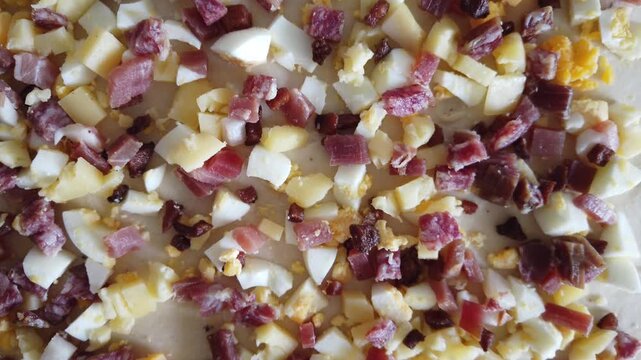 Dough layer scattered with diced hard-boiled eggs, chopped salami and grated cheese as a pastry topping, conveying homemade cooking, brunch preparation and rustic comfort food.