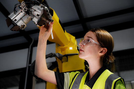 A female engineer inspects robotic arm components in a mechanical engineering factory. These robots are used in large-scale factories.