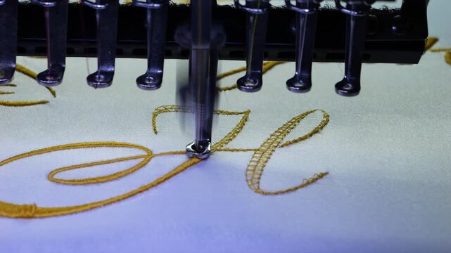 Machine embroidery of the initial "H" with gold thread on a white satin robe. Preparation for the wedding day. Elegant bridal lingerie. Close-up.