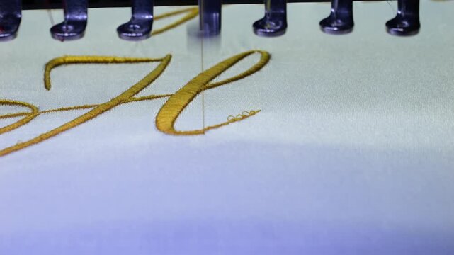 Machine embroidery of the initial "H" with gold thread on a white satin robe. Preparation for the wedding day. Elegant bridal lingerie. Close-up.