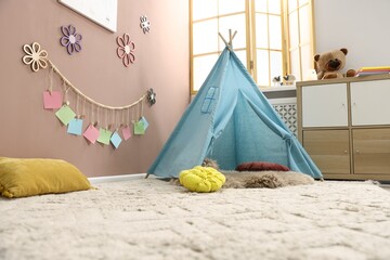 Colorful paper notes and beautiful decor hanging on beige wall near toy wigwam in stylish children's room. Interior design © New Africa