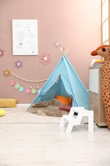 Colorful paper notes and beautiful decor hanging on beige wall near toy wigwam in stylish children's room. Interior design © New Africa
