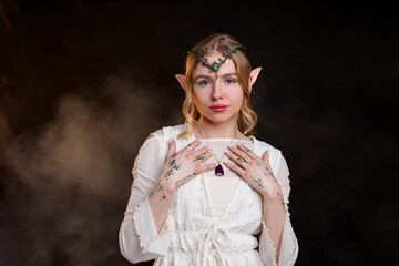 Fototapeta premium Beautiful girl dressed as elf on black background with smoke