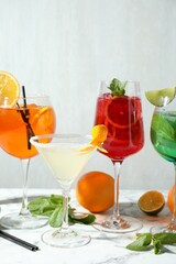 Fototapeta premium Different tasty refreshing cocktails in glasses, fresh citrus fruits and mint on light marble table, closeup