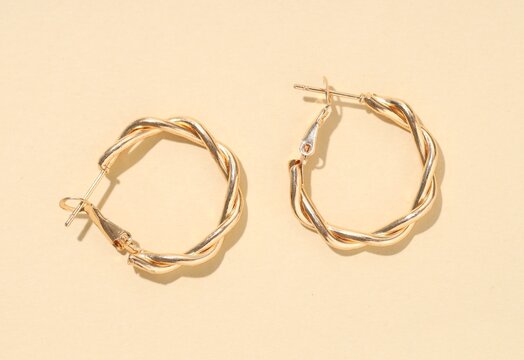 Pair of golden earrings on beige background, flat lay