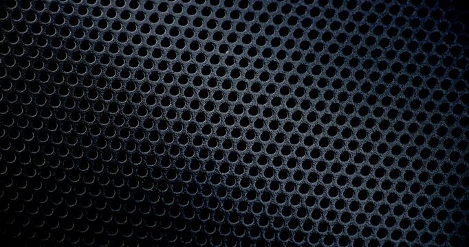 Black Perforated Metal Mesh. Smooth slow movement across extreme close-up of dark perforated metal grid with dramatic side lighting.