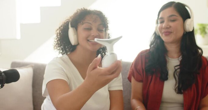 Female duo watching left host extending white device to camera, showing T metal head for recording