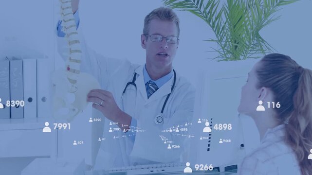 Male doctor raising spine model and explaining issue to patient, medical overlay marking vertebrae