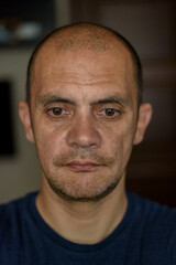 Fototapeta premium Middle-aged man with short hair and facial hair, wearing a blue t-shirt, poses for a close-up portrait against a blurred background