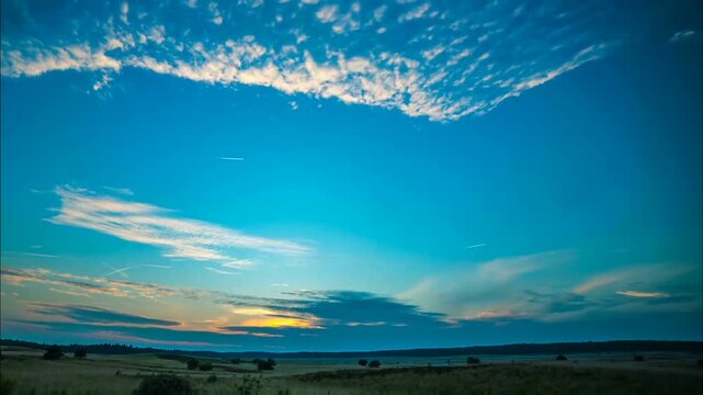 Rolling fields stretch toward the horizon under a breathtaking sky filled with textured clouds, where faint sunlight paints the landscape with soft, warm colors.