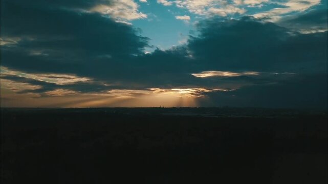 Golden sunlight pierces through dramatic clouds, illuminating a distant cityscape over a dark, silhouetted landscape, creating a breathtaking and atmospheric vista.