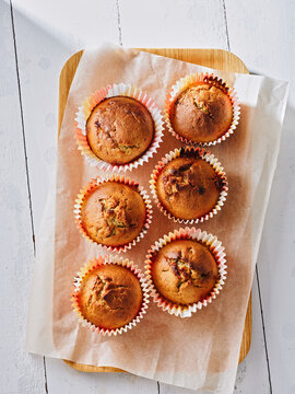 Six freshly baked muffins are arranged on a wooden board lined with parchment paper. Ideal for use in restaurant menus, food blogs, and promotional content for bakeries