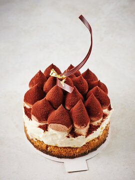 This image features a beautifully crafted tiramisu cake topped with chocolate mousse peaks and a decorative ribbon. Ideal for menus, bakery displays, social media posts, and celebrations