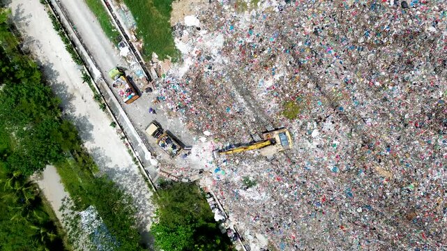 Large scale landfill operation with excavator and garbage trucks working at waste disposal site