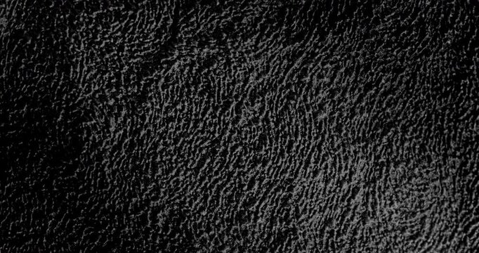 Abstract black texture. The slow, smooth diagonal movement of a dark, rough surface moving in a soft beam of light.