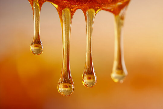 Golden thick liquid honey slowly dripping down in elongated droplets with warm amber background creating a rich natural texture close-up view