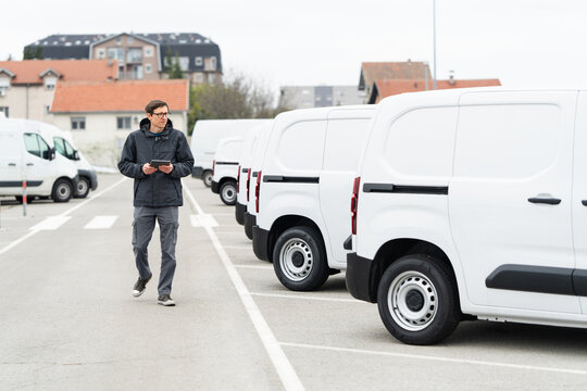 Fleet manager with digital tablet supervising rows of white delivery vans