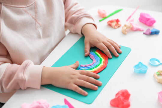 Little girl playing with colorful play dough at white table, closeup