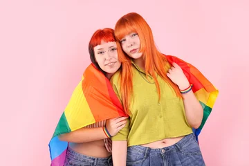 Lovely lesbian couple with rainbow flag on pink background. LGBT concept © New Africa