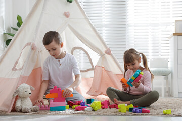 Little kids playing with building blocks near toy wigwam at home © New Africa