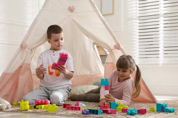 Little kids playing with building blocks near toy wigwam at home © New Africa