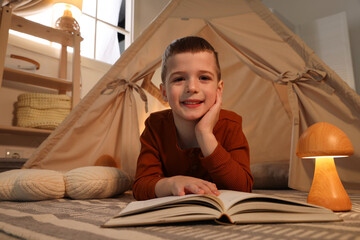 Little boy reading book near toy wigwam at home © New Africa