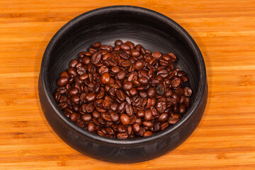 Fototapeta premium Roasted coffee beans in black clay bowl on wooden surface