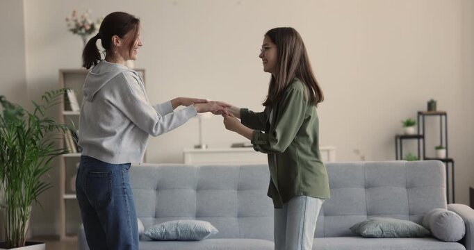 Caucasian mother and daughter dancing to favourite music in living room, jumping, having tun together on active weekend leisure at home. Friendly relationship between teen and parent, joy, family time