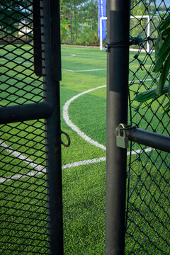 Padlock secured on black fence gate of mini soccer field surrounded by lush trees