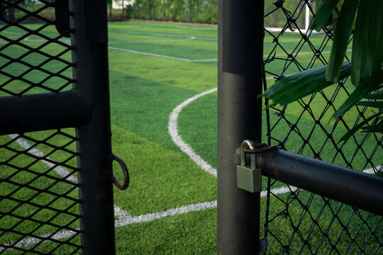 Padlock secured on black fence gate of mini soccer field surrounded by lush trees